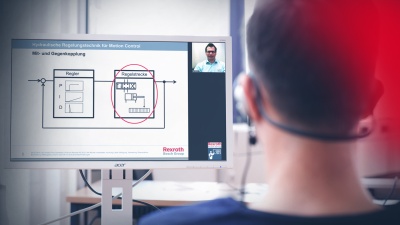 Participant of an online training sits in front of a PC and completes a course. The trainer is connected via video conference and explains the learning content.
