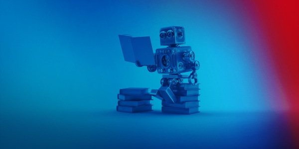 Zabawkowy robot Humanuider siedzi na stosie książek i czyta.