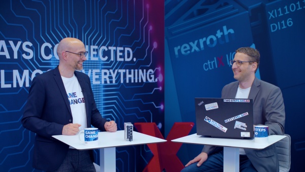 Gastgeber Christian Zentraf und sein Gast Kai Müller stehen an Besprechungstischen und sprechen über das Konfigurieren einer Handling-Applikation mit der ctrlX CORE, der Steuerungshardware der Automatisierungslösung ctrlX AUTOMATION