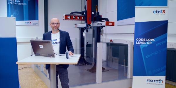 Gospodarz Christian Zentraf stoi przy stole konferencyjnym i pokazuje na żywo jak rozwiązanie automatyzacji ctrlX AUTOMATION kontroluje i napędza aplikację pick-and-place