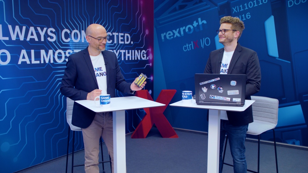 Host Christian Zentraf and his guest Christoph Büttner stand at meeting tables and talk about ctrlX SAFETY, the safety mini controller of the automation solution ctrlX AUTOMATION