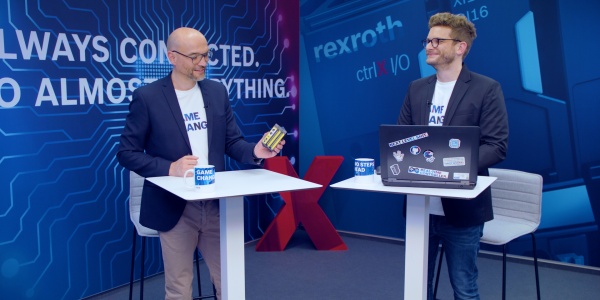 Gospodarz Christian Zentraf i jego gość Christoph Büttner stoją przy stołach i rozmawiają o ctrlX SAFETY, mini sterowniku bezpieczeństwa rozwiązania automatyzacji ctrlX AUTOMATION.