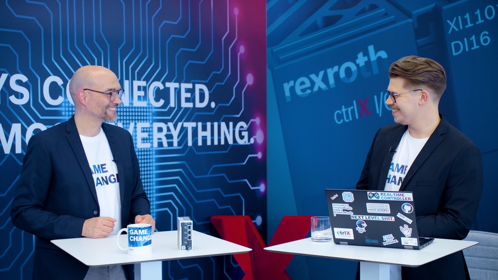 Gospodarz Christian Zentraf i jego gość Benedikt Rüb stoją przy stołach i rozmawiają o ctrlX Configurator, narzędziu konfiguracyjnym rozwiązania automatyzacji ctrlX AUTOMATION.