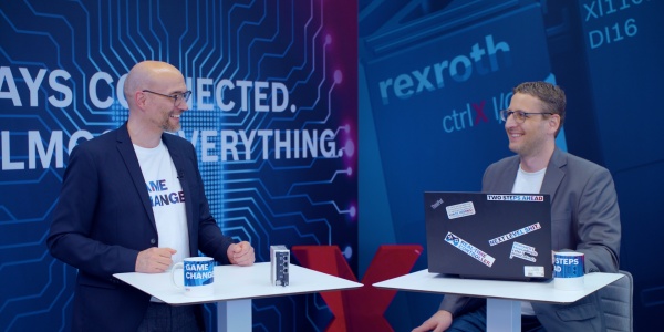 Gospodarz Christian Zentraf i jego gość Kai Müller stoją przy stołach konferencyjnych i opowiadają o konfiguracji aplikacji przeładunkowej za pomocą ctrlX CORE, sprzętu sterującego rozwiązania automatyzacji ctrlX AUTOMATION.