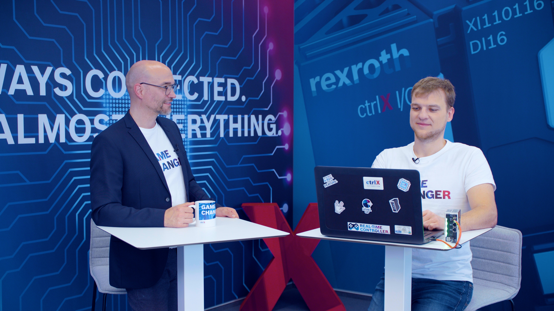 Host Christian Zentraf and his guest Michael Schäfer stand at meeting tables and talk about programming Python scripts directly on the ctrlX CORE, the control hardware of the automation solution ctrlX AUTOMATION
